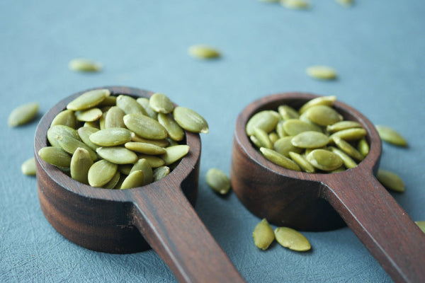 Green pumpkin seeds in wooden spoons on a table surface