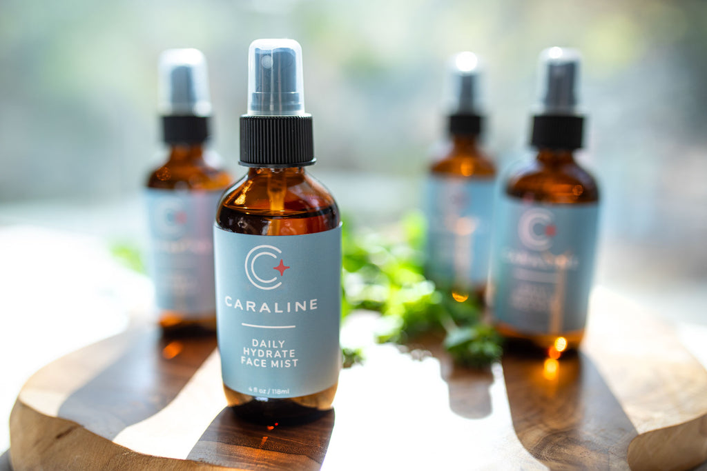 Multiple bottles of Caraline Skincare Daily Hydrate Face Mist on a wooden board