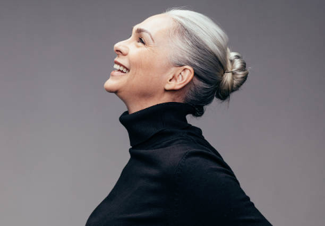 Attractive older woman with gray hair in a bun wearing a black turtleneck and smiling