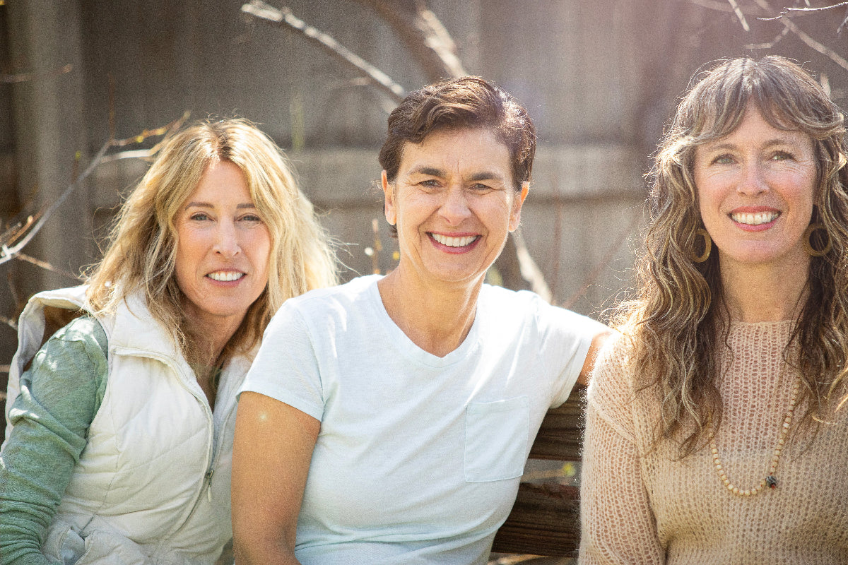 Three women in their 50s on  bench outside looking at the camera